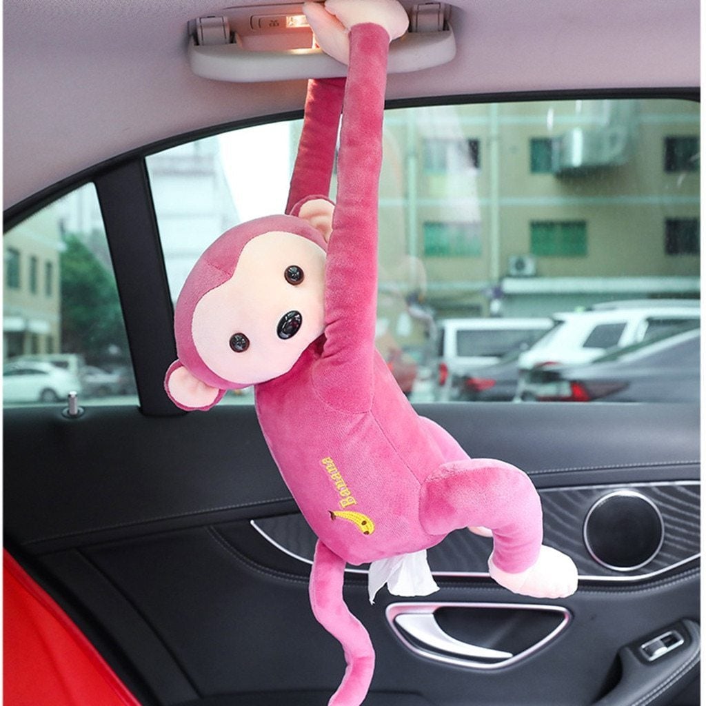 Pink plush hanging monkey tissue holder with soft fabric, embroidered yellow banana, and black button eyes on car sun visor