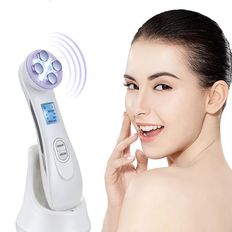 White handheld 5-in-1 face massager device with four glowing purple treatment heads and a digital display screen
