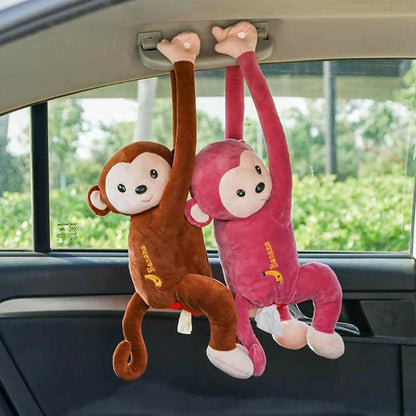 Two plush hanging monkey tissue holders in brown and pink with embroidered details hanging from a car visor