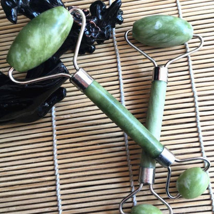Two jade green double head jade face rollers with polished stone heads and metallic handles for facial massage